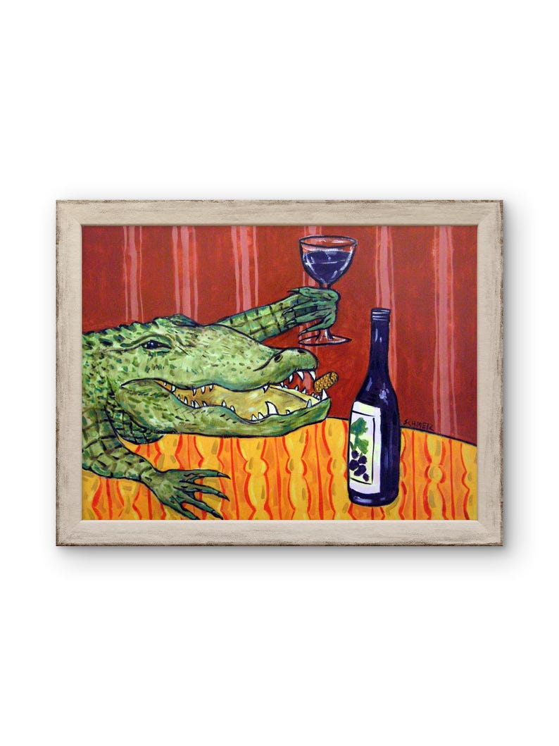 May include: A framed painting depicts a green alligator with an open mouth holding a wine glass in one claw. A wine bottle with a grape label sits on an orange patterned tablecloth against a red striped background. The artist signature is visible.