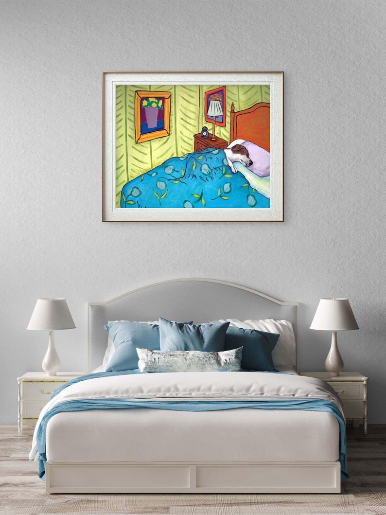 May include: A framed art print depicting a bedroom scene with a dog sleeping under a blue floral patterned blanket. The illustration features a bed with a headboard, a nightstand with a lamp, and a framed picture on a light green wall.