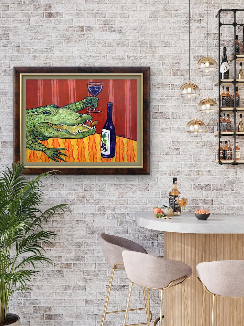 May include: A framed painting depicting a green alligator sitting at a table with an orange patterned tablecloth. The alligator holds a glass of red wine in one claw and has a bottle of wine with a grape label sitting next to it on the table.