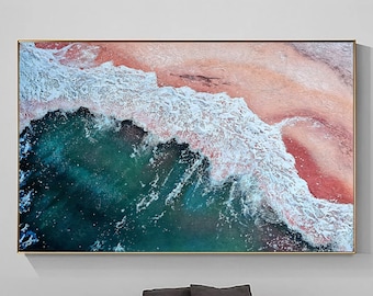May include: An aerial photograph of a beach with turquoise water and white waves crashing on the shore. The sand is a light pink color.