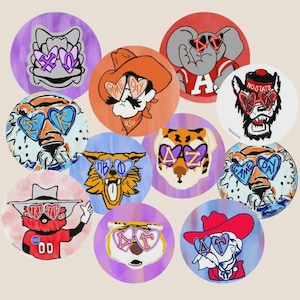 May include: A collection of round stickers featuring cartoon illustrations of animals and figures wearing heart-shaped sunglasses. Each sticker has a unique design, including a tiger, elephant, and cowboy, with various Greek letters and the words "GAME DAY" on the sunglasses.