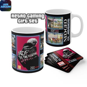 Op de afbeelding: Een witte keramische mok en een stapel vierkante onderzetters met Neo Geo KOF 02 Be The Fighter graphics. De mok toont een personagesilhouet op een rode achtergrond met de tekst Neo Geo Classics en KOF 02 Be The Fighter.