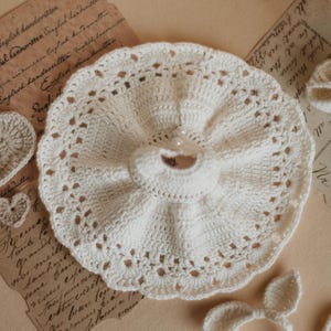May include: A white crocheted dress with a ruffled skirt and a pearl embellishment. The dress is handmade and has a delicate lace trim.