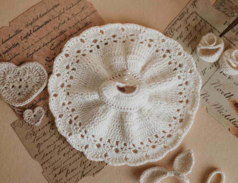 May include: A white crocheted dress with a ruffled skirt and a pearl embellishment. The dress is handmade and has a delicate lace trim.