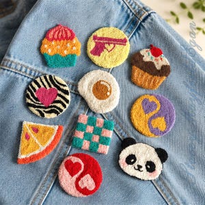Può includere: Una collezione di dieci toppe ricamate con vari disegni, tra cui un cupcake, un cerchio giallo con una pistola rosa, un cupcake al cioccolato, un cuore zebrato, un uovo al tegamino, uno yin-yang viola e giallo, una fetta di agrume, un quadrato a scacchi, un panda e un cuore rosso.
