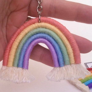 May include: A rainbow-coloured keychain made of yarn with a white tassel on each end. The keychain is attached to a silver metal ring.