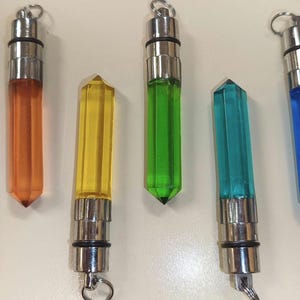 Può includere: Otto pendenti traslucidi a forma di cristallo esagonale in vari colori, tra cui rosa, rosso, arancione, giallo, verde, verde acqua, blu e viola. Ogni pendente presenta un tappo in metallo color argento con un piccolo anello circolare.