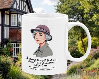 Op de afbeelding: Een witte keramische mok met een citaat uit de tv-serie "Ze doen het met spiegels" met een cartoonillustratie van het hoofdpersonage van de serie, Miss Marple. Het citaat luidt: "Ik heb altijd gedacht dat je moet zien en observeren, niet alleen zien. Ze doen het met spiegels."
