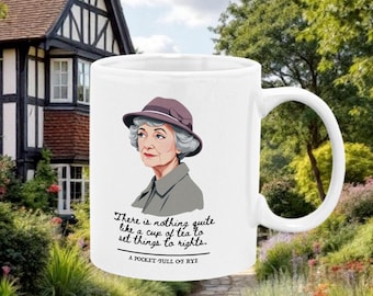 Op de afbeelding: Witte keramische mok met een cartoonillustratie van een vrouw met grijs haar en een paarse hoed. De mok heeft de tekst "There is nothing quite like a cup of tea to set things to rights." en "A POCKET FULL OF RYE" erop gedrukt.