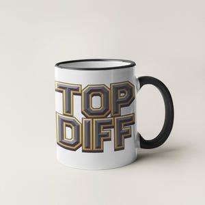 May include: White ceramic mug with a black rim and handle. The mug has the words "TOP DIFF" printed on it in gold and gray letters.