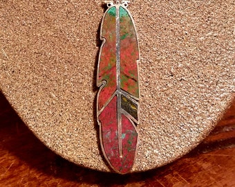 May include: A silver necklace with a red, green, and black gemstone feather pendant.