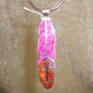 K&ouml;nnte beinhalten: Eine silberne Halskette mit einem rosa und orangefarbenen Federnanh&auml;nger. Die Feder ist aus Naturstein gefertigt und hat ein detailliertes Design.