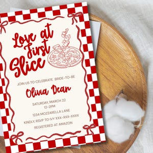 May include: A rectangular invitation card featuring a red and white checkered border and a cream-coloured centre. The text reads Love at First Slice, Join us to celebrate bride-to-be Olivia Dean, Saturday, March 22, 12-2pm, 1234 Mozzarella Lane.