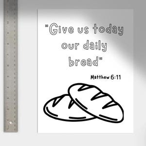 May include: Black and white illustration of two loaves of bread with the text "Give us today our daily bread" and "Matthew 6:11". The image is on a white background with a metal ruler on the left side.