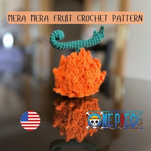Könnte beinhalten: Gehäkelte orange Frucht mit grünem Stiel, die an die Mera Mera no Mi aus dem Anime One Piece erinnert. Die Frucht spiegelt sich auf einer Oberfläche mit dem One Piece-Logo.