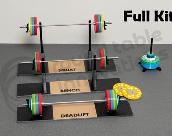 May include: A miniature weightlifting set with three different weightlifting stations: squat, bench, and deadlift. Each station has a barbell with colourful weight plates. The set also includes a stand with additional weight plates.