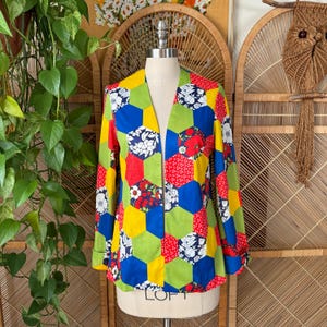 May include: A colorful patchwork jacket with a geometric pattern of hexagons in red, blue, yellow, green, and white floral prints. The jacket has long sleeves and a collarless design, displayed on a mannequin.
