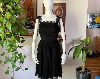 May include: A black lace dress with a ruffled skirt and a square neckline. The dress is sleeveless and has a fitted bodice.