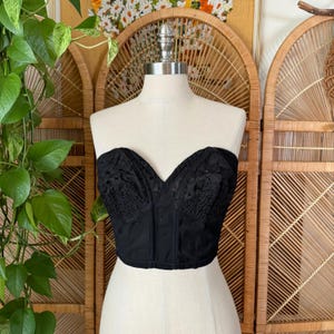 May include: A black strapless corset with a lace overlay and a boned bodice.
