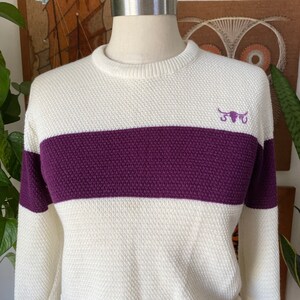 May include: White sweater with a purple horizontal stripe and a small embroidered bull's head logo.