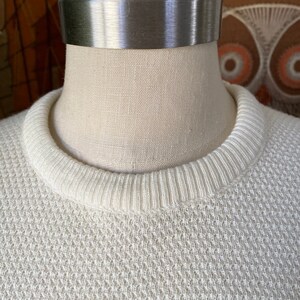 May include: A white knitted sweater with a ribbed neckline.