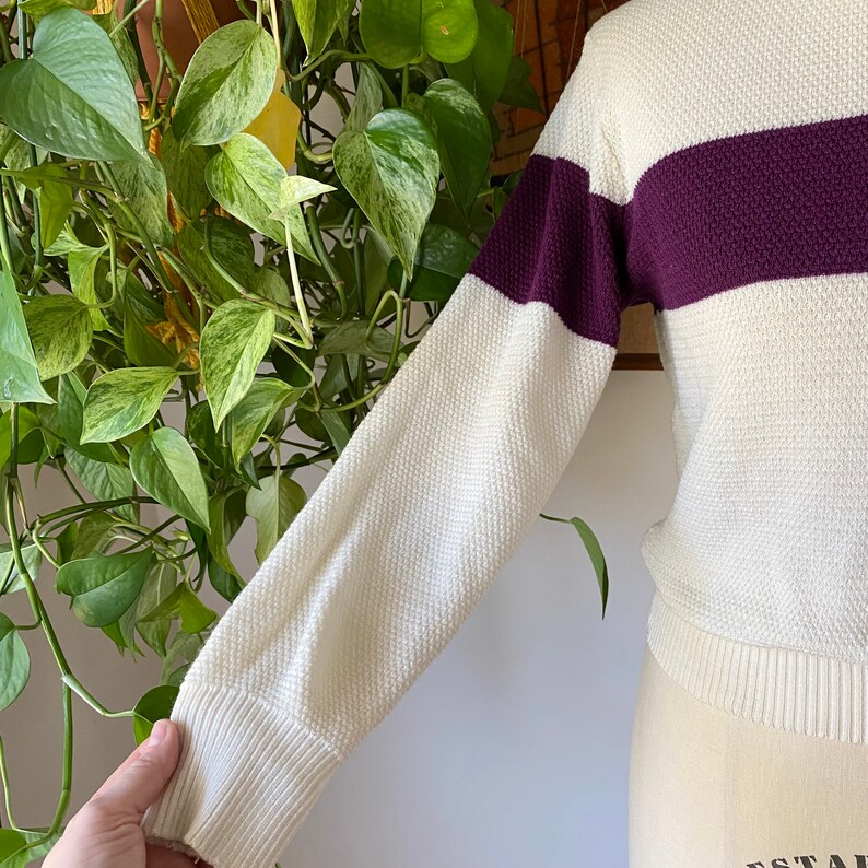 May include: A white and purple striped sweater with long sleeves. The sweater is made of a soft, knitted fabric.