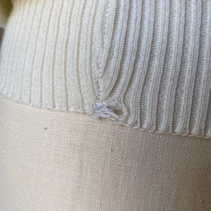 May include: Close-up of a white knitted sweater with a small hole in the fabric.