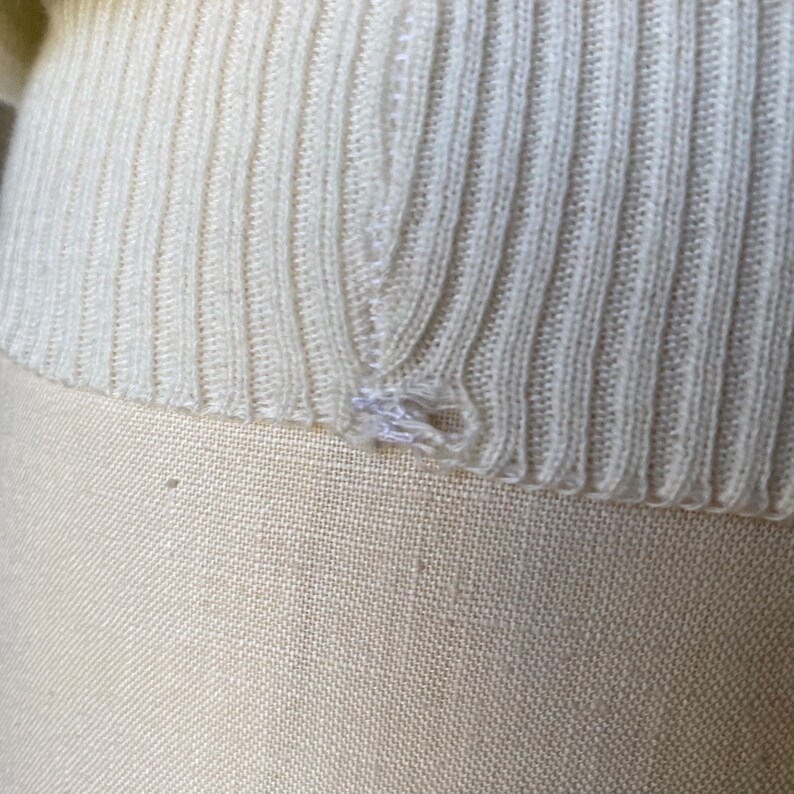 May include: Close-up of a white knitted sweater with a small hole in the fabric.