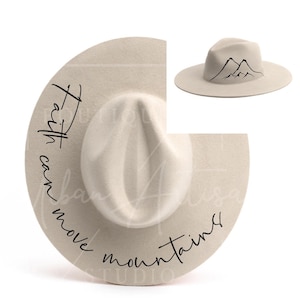 Puede incluir: Un sombrero fedora de fieltro beige con una silueta de montaña negra y el texto "Faith can move mountains" escrito en el borde.