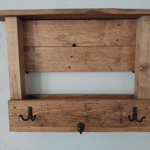 May include: Rustic wooden wall shelf with two hooks and a lower shelf. The shelf is stained a dark brown color and has a distressed look.