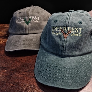 Peut inclure: Trois casquettes de baseball avec le texte "DEERFEST Bright Falls" et une silhouette de cerf brodée sur le devant. Les casquettes sont de différentes couleurs : gris, vert et marron.