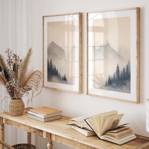 Può includere: Un tavolo console in legno con due stampe di paesaggi incorniciate di montagne e alberi. Il tavolo ha una finitura in legno chiaro ed è decorato con libri, un vaso di fiori secchi e un cesto di vimini.