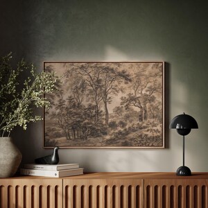 May include: A framed black and white drawing of a forest scene hangs on a green wall above a wooden dresser with a black lamp and a small black bird figurine.