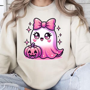 Peut inclure: Un sweat-shirt blanc avec un fant&ocirc;me rose paillet&eacute; portant un n&oelig;ud rose et tenant une citrouille rose. Le fant&ocirc;me a de grands yeux et une expression joyeuse.