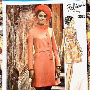 May include: A vintage Vogue Couturier Design fashion illustration featuring a woman in a coral-colored coat and hat. The design is by Fabiani of Italy, with the number 2325. The image has a retro aesthetic.