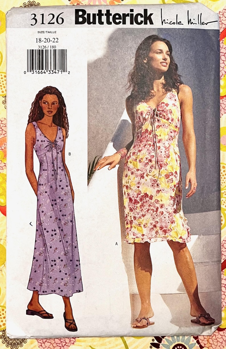 Op de afbeelding: Een Butterick naaipatroon met twee jurk ontwerpen. De ene jurk is een lavendelkleurige maxi met een kersenprint, de andere een bloemen knielange jurk. Het patroon bevat maten 18-22.