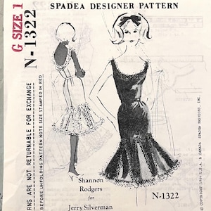 Può includere: Un cartamodello Spadea Designer N-1322 per un abito, taglia 16. La busta presenta un'illustrazione in bianco e nero di un abito con scollo rotondo e orlo a balze. Il testo include Shannon Rodgers per Jerry Silverman e copyright 1964.