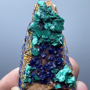 May include: A natural mineral specimen featuring a combination of vibrant colors. The piece showcases deep blue azurite crystals and bright green malachite formations, set against a brown matrix. The mineral has a rough, textured surface.