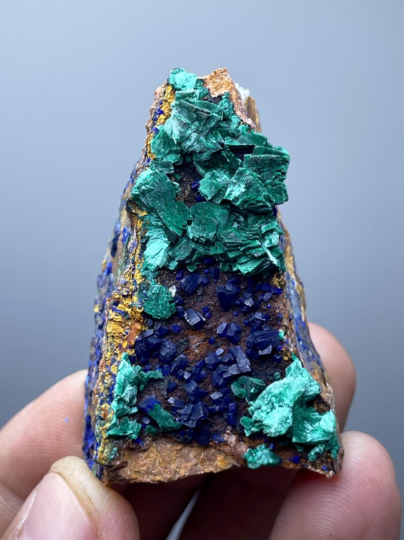 May include: A natural mineral specimen featuring a combination of vibrant colors. The piece showcases deep blue azurite crystals and bright green malachite formations, set against a brown matrix. The mineral has a rough, textured surface.