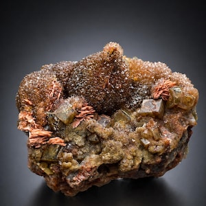 Könnte beinhalten: Nahaufnahme einer Mineralprobe mit rauer, strukturierter Oberfläche. Das Mineral weist eine Mischung aus Farben auf, darunter Braun, Orange und Grün. Kleine, kristallartige Strukturen bedecken Teile der Oberfläche.
