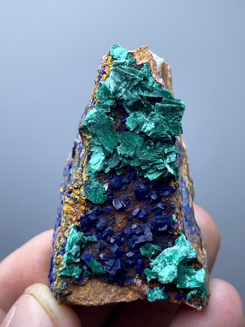 May include: A natural mineral specimen featuring a mix of colors. The rock has a brown base with patches of vibrant green and deep blue crystals. Yellow and gold accents are also visible, creating a striking contrast.
