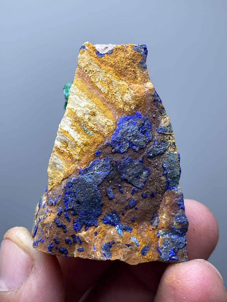 May include: A rough-cut mineral specimen featuring a mix of colors. The rock has a base of brown and tan hues, with striking patches of deep blue. The texture appears rough and natural, showcasing the mineral's raw beauty.