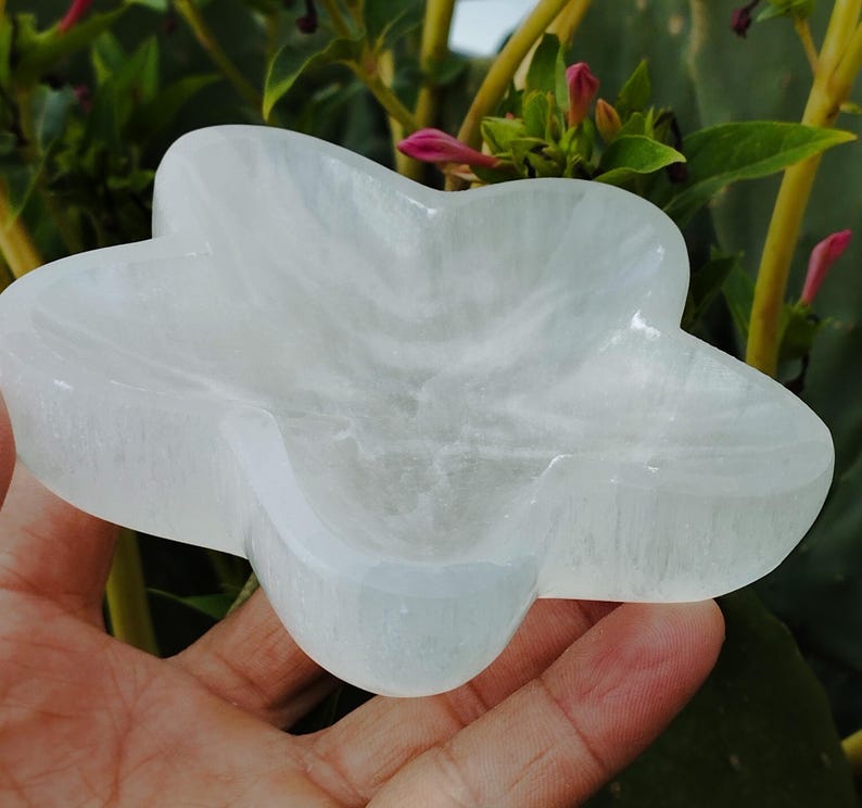May include: A white selenite star-shaped dish. The dish is carved from a single piece of selenite and has a smooth, polished surface.