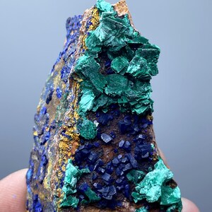 May include: A natural mineral specimen featuring a combination of vibrant colors. The piece showcases deep blue azurite crystals, contrasted by bright green malachite formations. The mineral is set against a backdrop of earthy brown and gold hues.