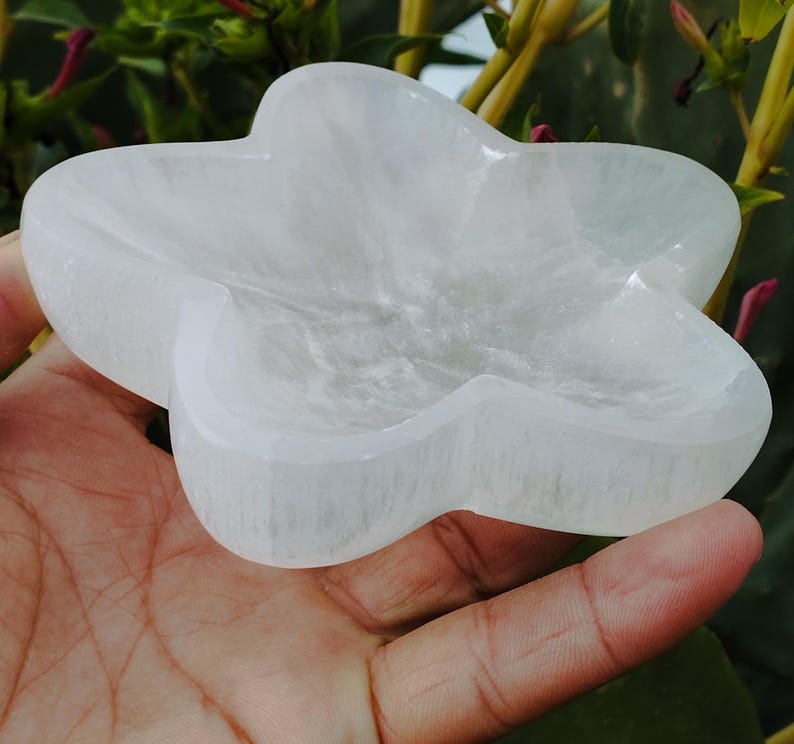 May include: A white selenite star-shaped dish. The dish is made of natural selenite crystal and has a smooth, polished surface.