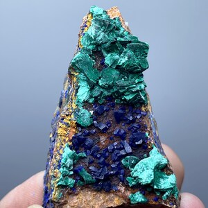 May include: A natural mineral specimen featuring a combination of colors and textures. The rock displays a mix of deep blue, vibrant green, and golden-brown hues. The surface is covered with crystalline formations.