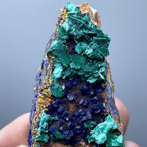 May include: A natural mineral specimen featuring a combination of colors and textures. The rock displays deep blue azurite crystals, vibrant green malachite, and a golden-brown matrix. The mineral formation is a striking example of natural artistry.