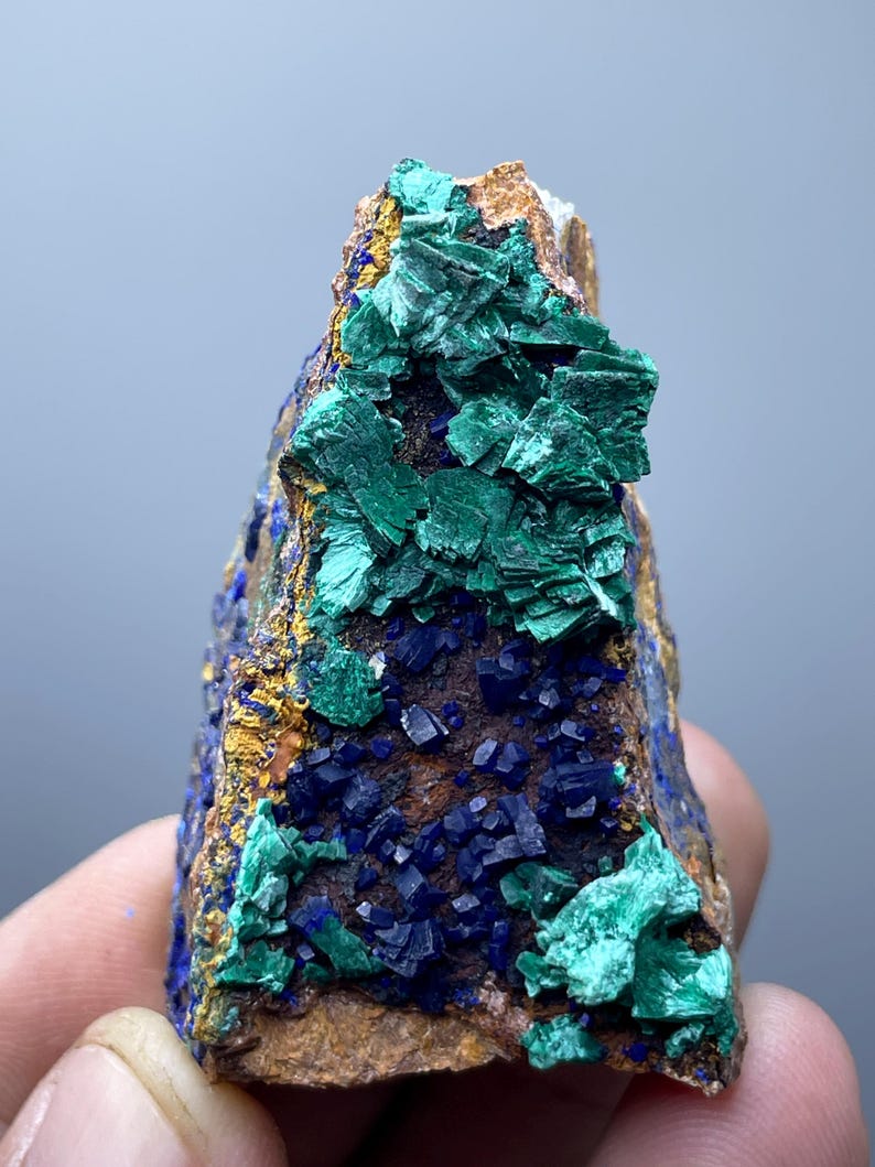 May include: A natural mineral specimen featuring a combination of colors and textures. The rock displays deep blue azurite crystals, vibrant green malachite, and a golden-brown matrix. The mineral formation is a striking example of natural artistry.