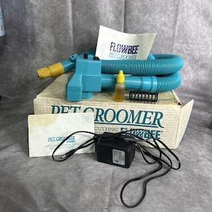 May include: A vintage Flowbee Pet Groomer kit. The kit includes a teal grooming tool, a coiled teal hose, a power adapter, a small bottle, and a box with the text "DET GROOMER CUTTING FLOWBEE".