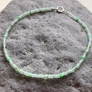 May include: A beaded bracelet featuring a repeating pattern of translucent light green glass beads, opaque mint green round beads, and small clear spacer beads, finished with a silver-toned metal lobster claw clasp and a circular jump ring.